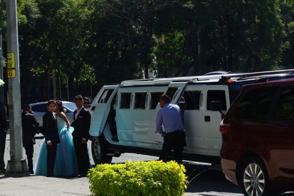Girl in ball gown with young male attendants, and a stretch Hummer limo.